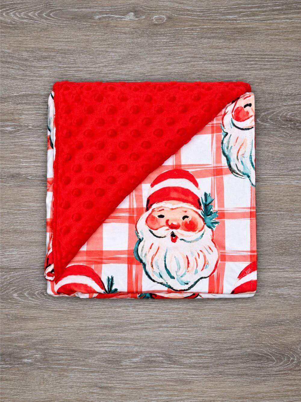 Santa Christmas plaid baby blanket with red minky dot backing spread out beneath a seated baby