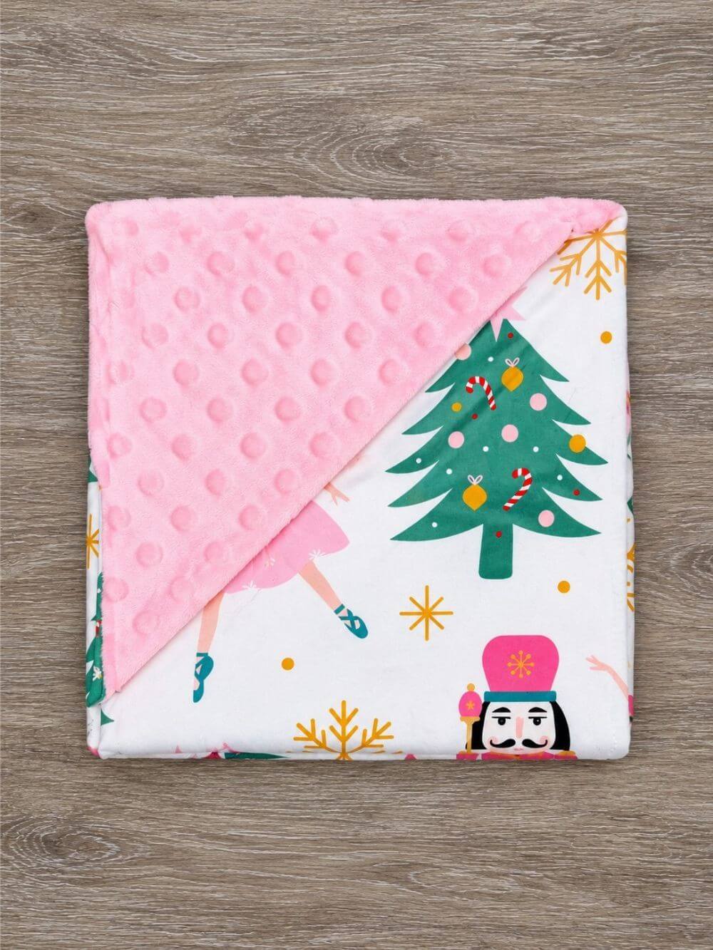 Pink nutcracker and Christmas tree baby blanket with pink minky dot backing folded to show the patterned front and reverse
