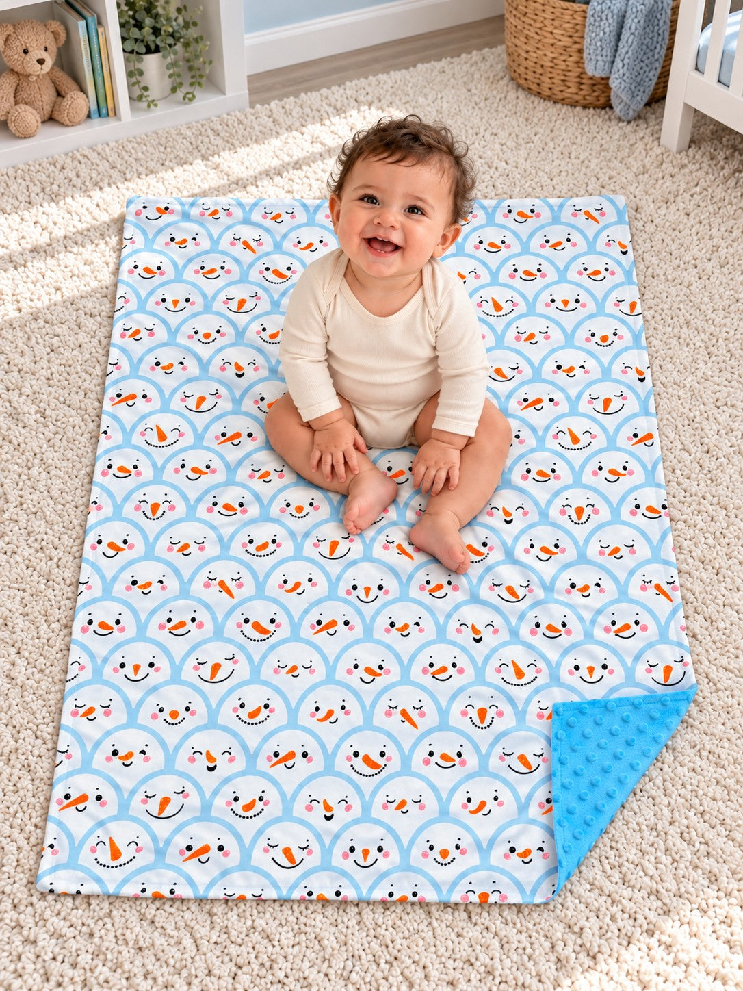 Blue snowman baby blanket with blue minky dot backing spread on the floor beneath a baby, viewed from above